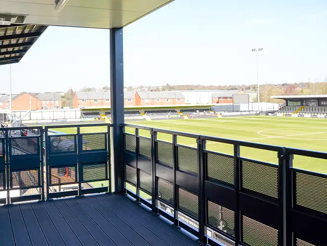 View from the balcony of a modular unit by S Jones Containers at Hednesford Town Football Club, overlooking the football pitch and stadium seating, with safety railings and covered roofing visible.