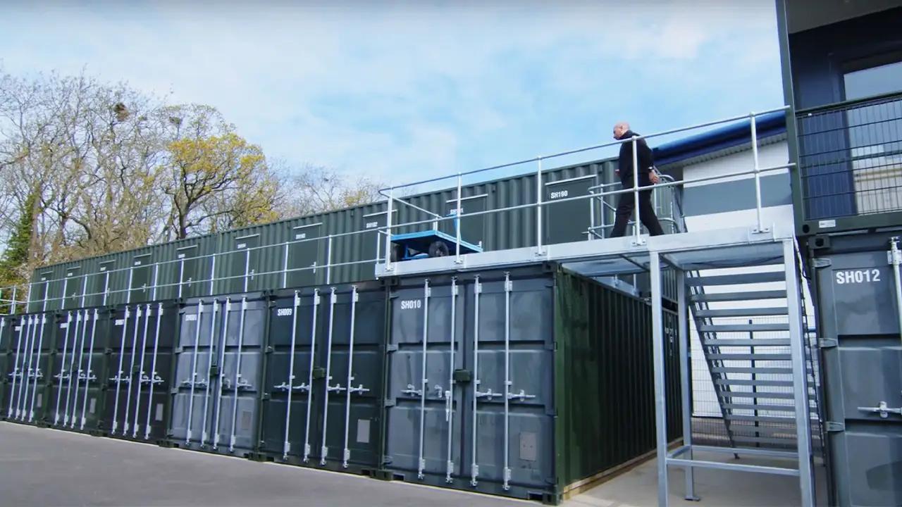 Multi store container unit installed above standard storage containers with secure access staircase and walkway at a self storage site in Great Britain.