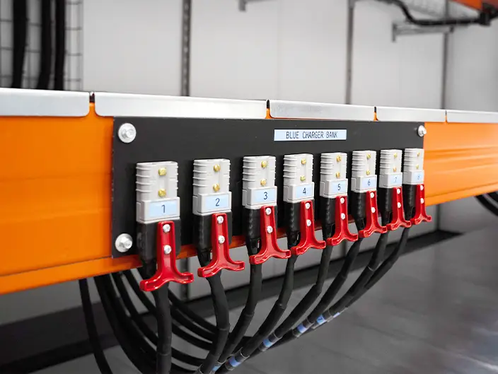 Close-up view of a battery charger bank inside a converted shipping container, showing labelled charging ports and connected power cables
